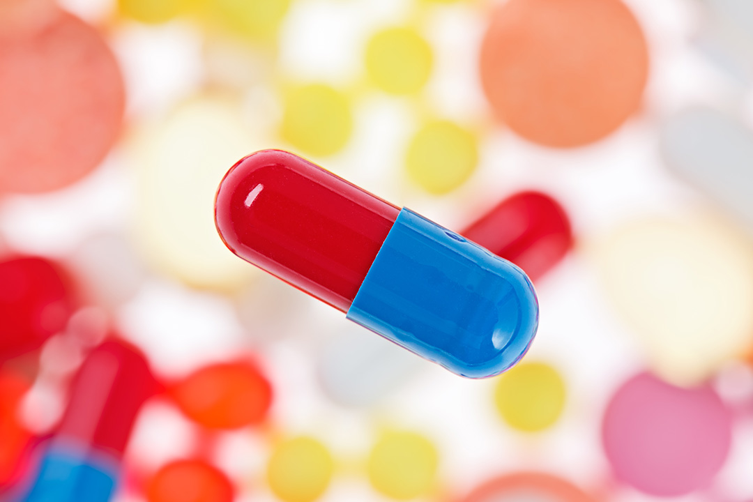 One capsule (pill) macro view on blurred multicolored drugs background, medical concept